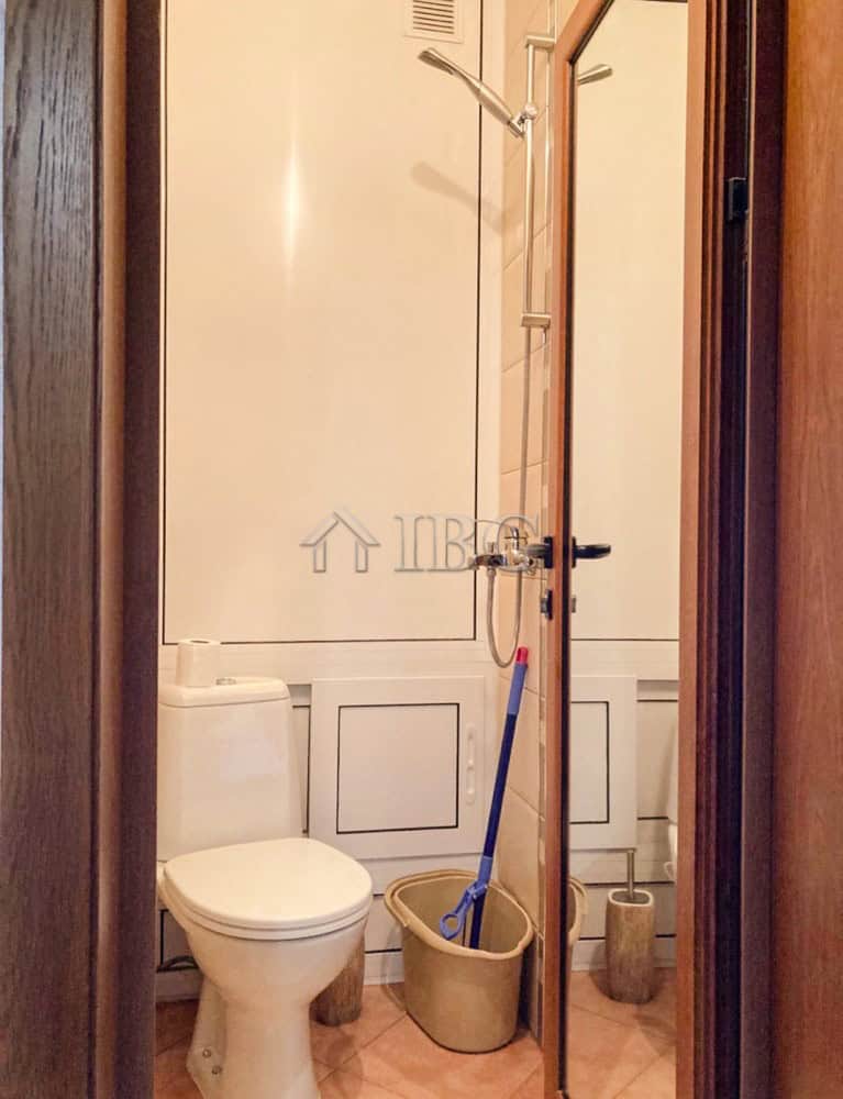 Cozy Bathroom in Ruse Apartment Small bathroom with toilet, shower, and cleaning tools in a Ruse apartment.