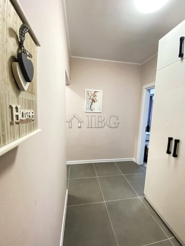 Bright hallway with white walls, gray tiles, and a large white wardrobe in a modern apartment.