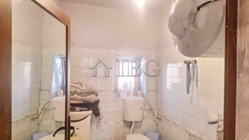 Small bathroom with white tiles, mirror, and washing area in a quiet residential setting.