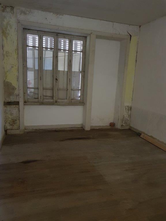 Interior view of a partially renovated apartment with wooden flooring and large window.