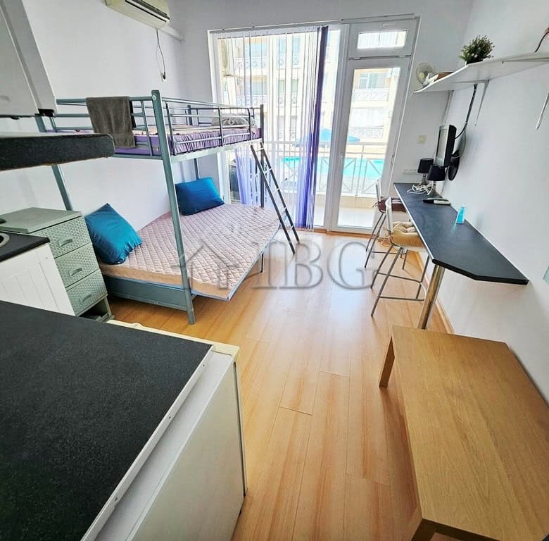 Bright studio apartment with balcony overlooking pool and sunny beach scenery.