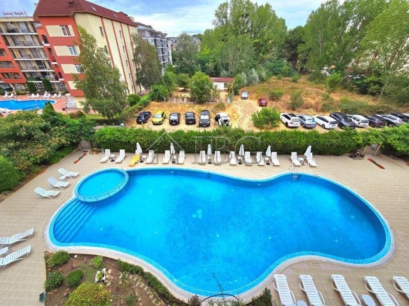 Pool view of a 1-bedroom apartment with a large outdoor swimming pool and sun loungers.