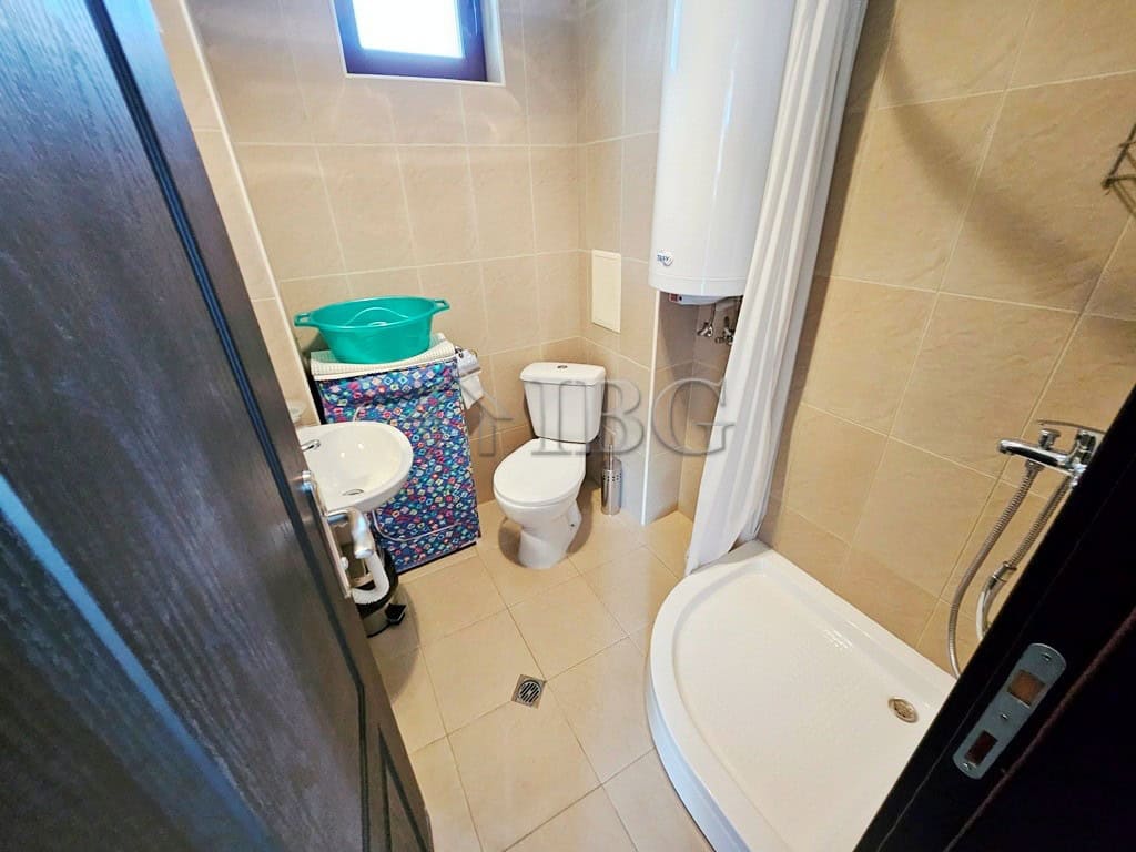 Bathroom with shower, toilet, and water heater in a sunny beach apartment.
