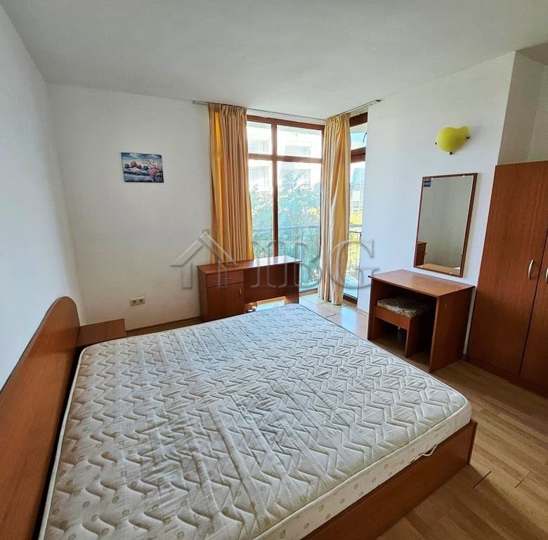 Spacious bedroom with a large window, wooden bed frame, wardrobe, and dressing table in a sunny apar.