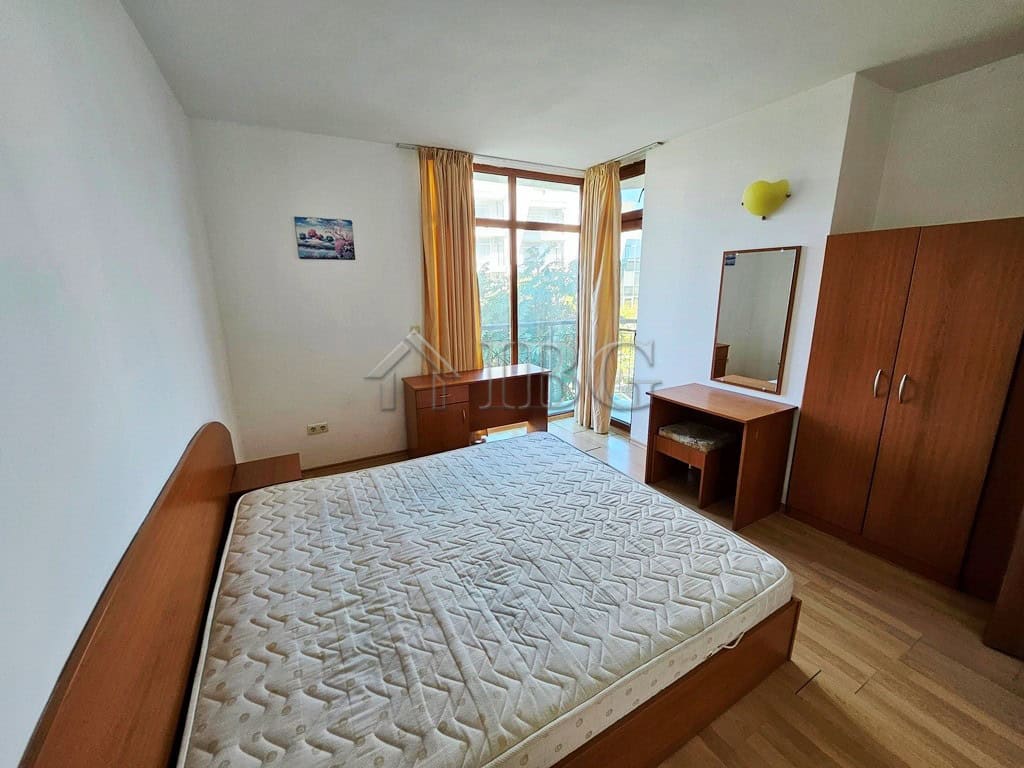Modern bedroom with large window and wooden furniture in Blue Summer Complex. Spacious bedroom with a large window, wooden bed frame, wardrobe, and dressing table in a sunny apar.
