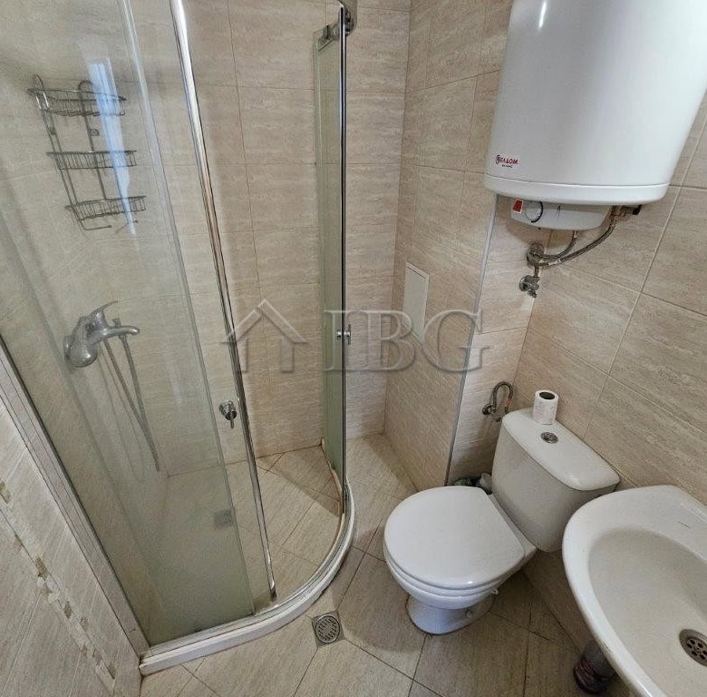 Bathroom with shower, toilet, and sink in a sunny beach studio apartment.