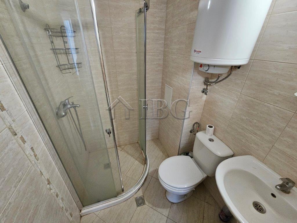 Bathroom with shower, toilet, and sink in a sunny beach studio apartment.
