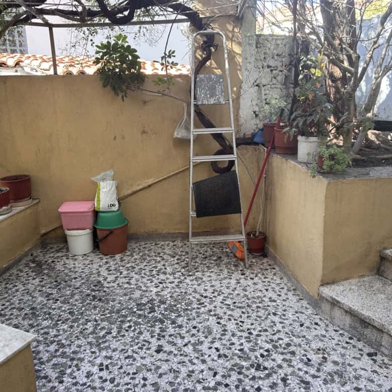 Outdoor terrace with potted plants, garden tools, and a ladder in a residential setting.