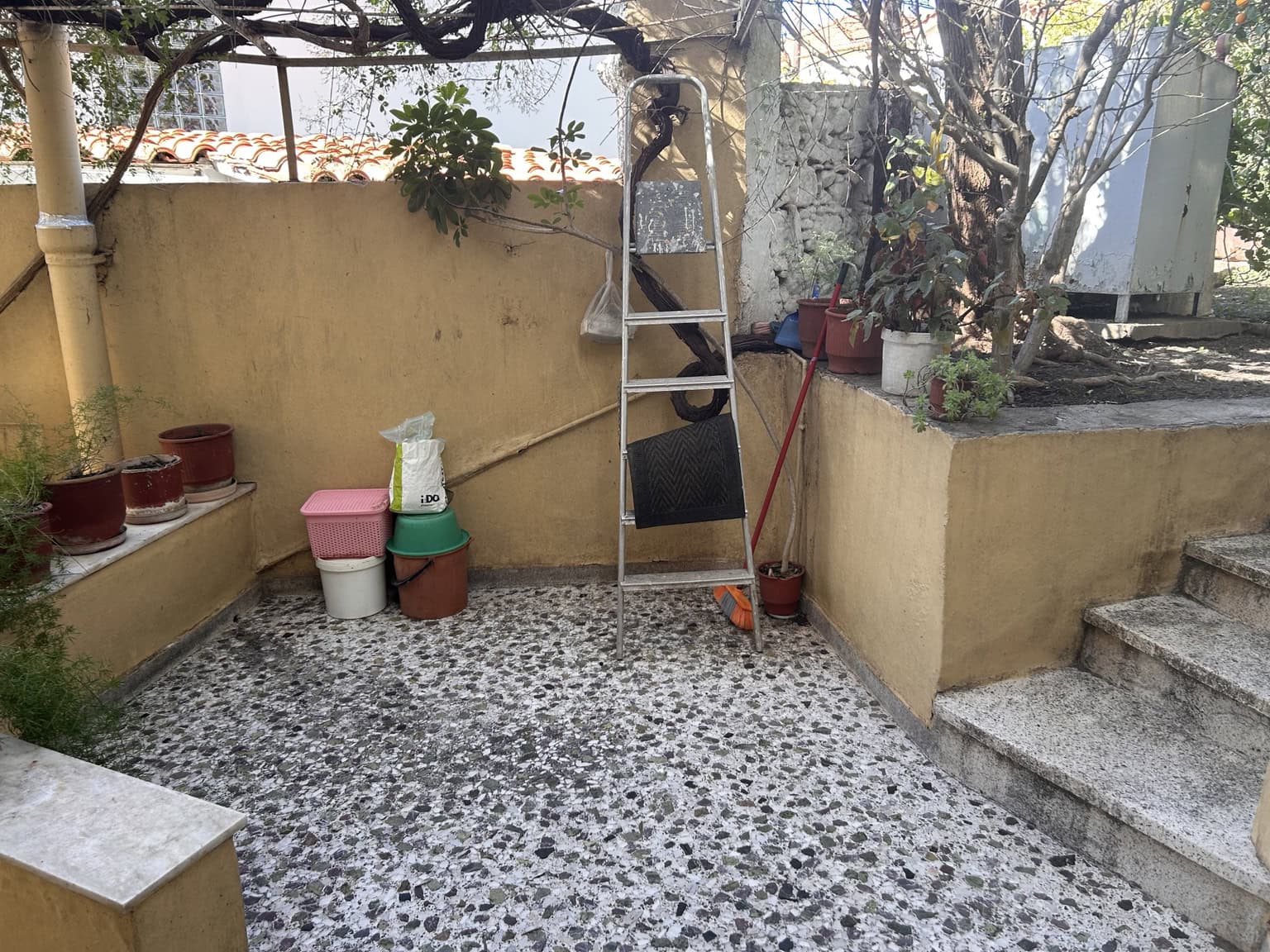 Outdoor terrace with potted plants, garden tools, and a ladder in a residential setting.