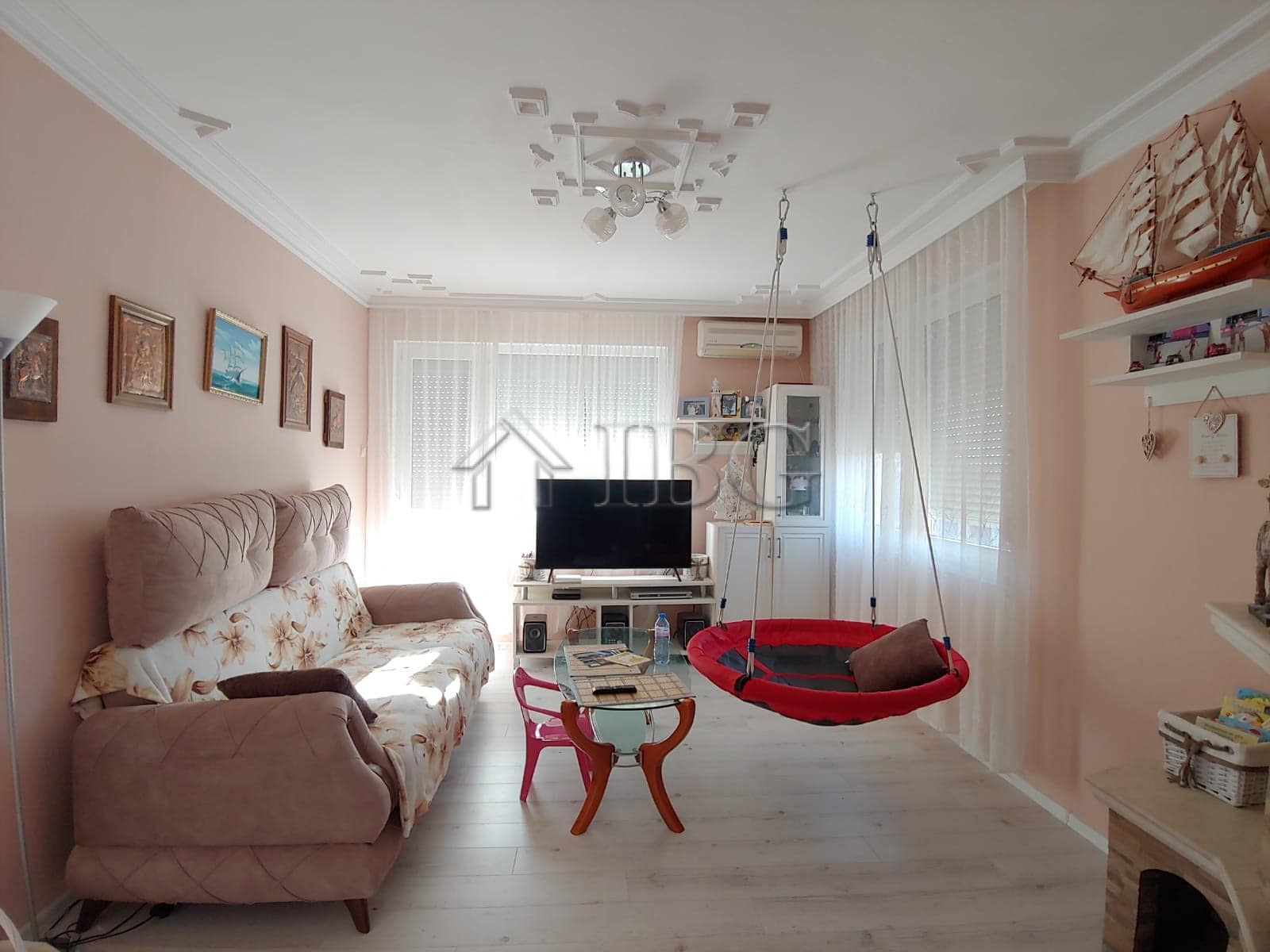 Bright living room with sofa, TV, and cozy swing in Kosharitsa home.