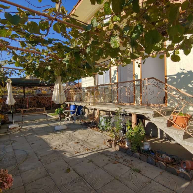 Bright outdoor patio of a large house in Kosharitsa, featuring lush greenery and a cozy seating area.