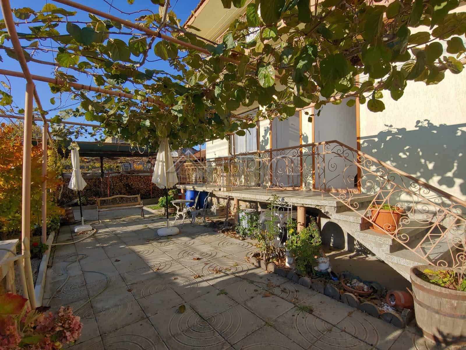 Bright outdoor patio of a large house in Kosharitsa, featuring lush greenery and a cozy seating area.