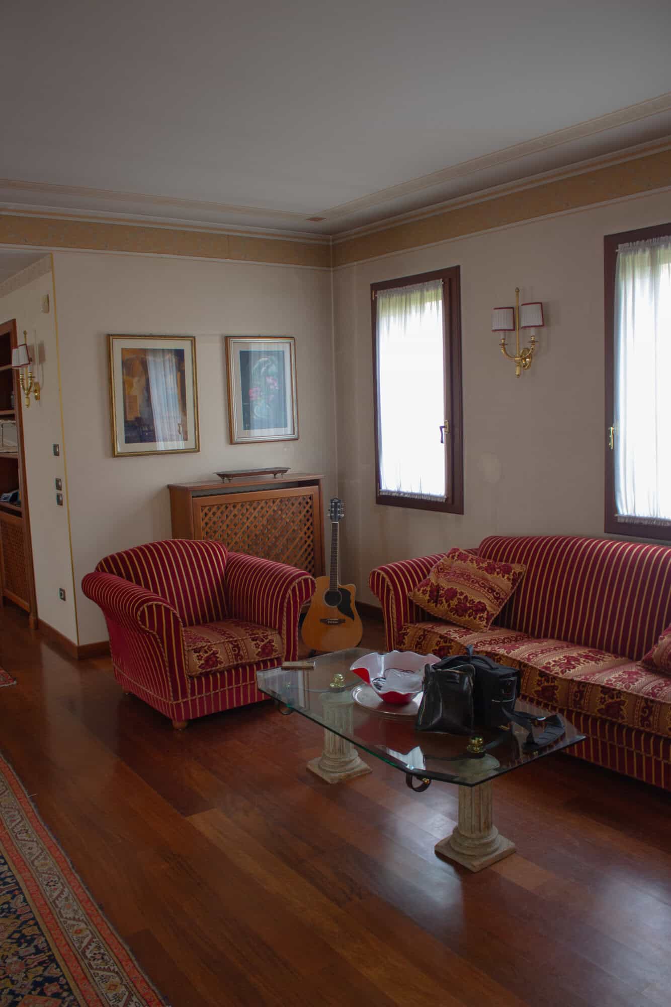 Spacious living room featuring classic furniture, artwork, and natural light from large windows.