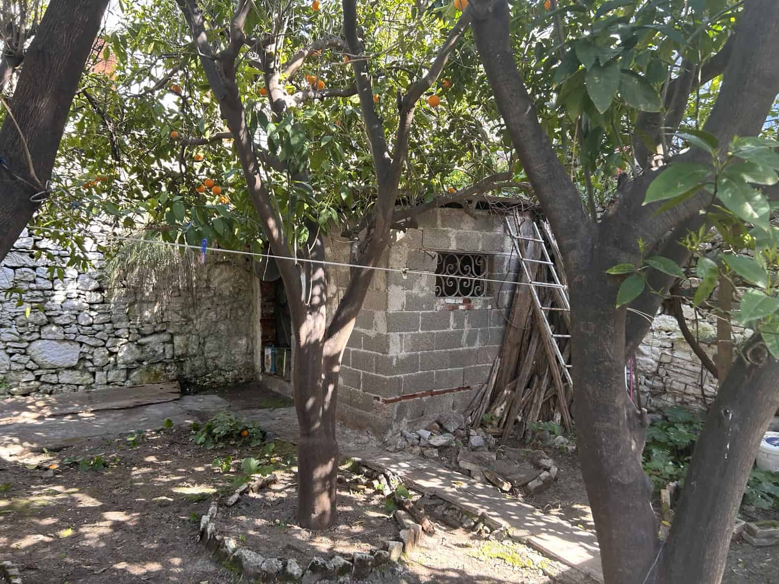 Small rustic house with trees and stone wall in a rural setting, showcasing traditional construction.
