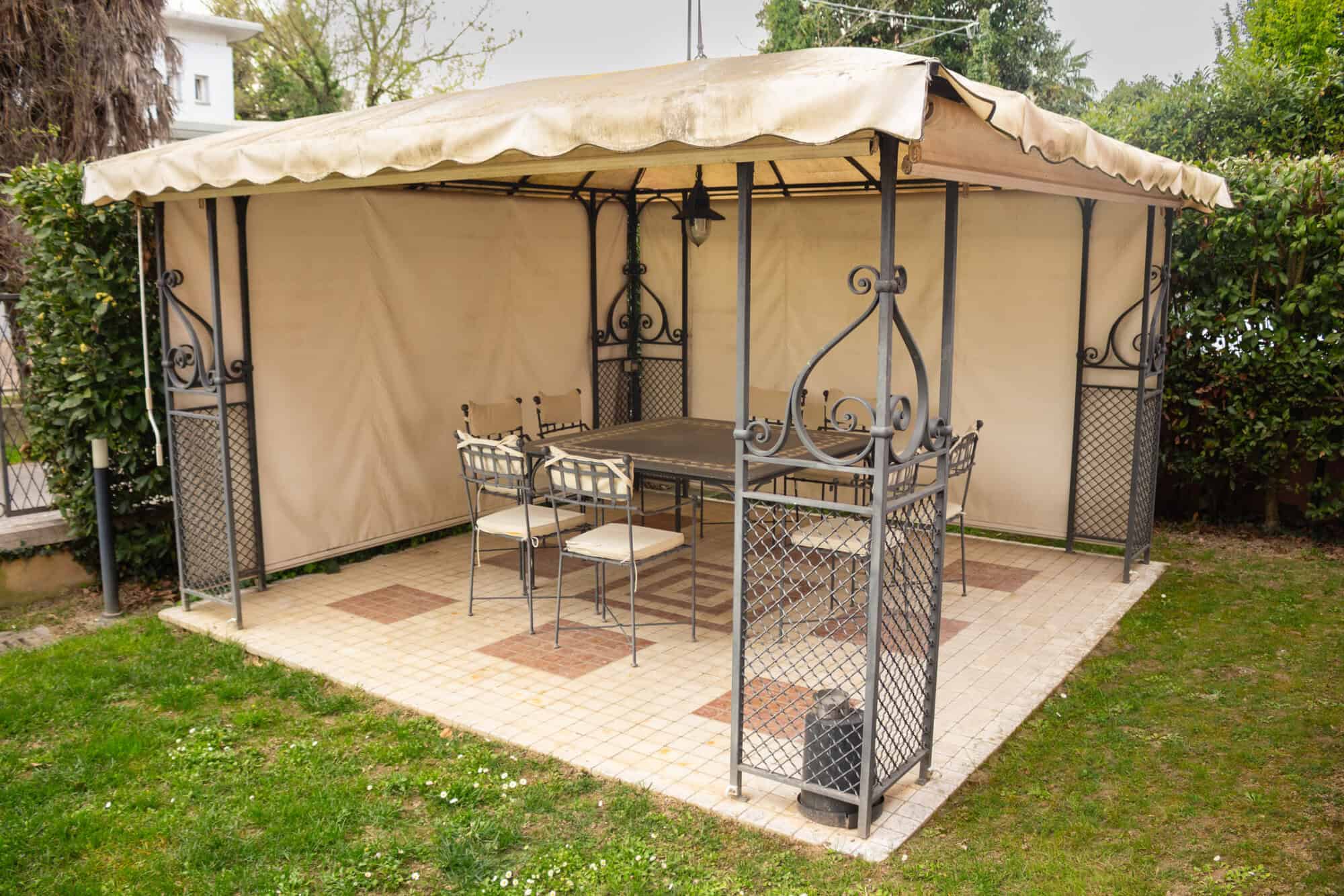 Outdoor garden gazebo with metal frame, beige canopy, and seating for outdoor relaxation.