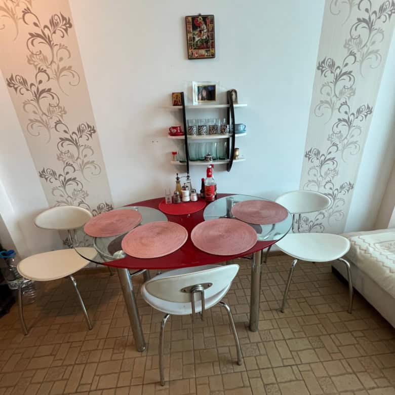 Interior of a dining space in a maisonette with a round table and colorful chairs, partial sea view.