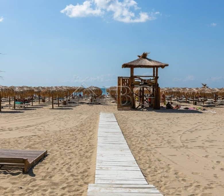 Beach scene with sun loungers, straw umbrellas, and a wooden walkway leading to the sea.