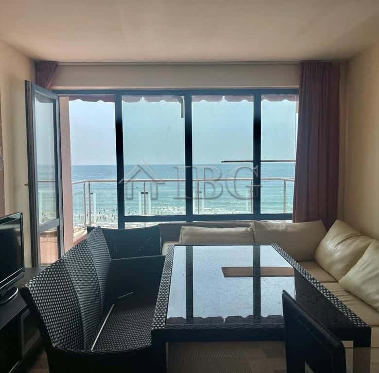 Modern living room with large windows overlooking sunny beach and ocean.
