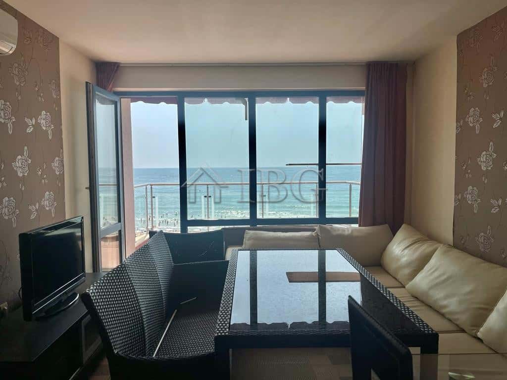 Modern living room with large windows overlooking sunny beach and ocean.