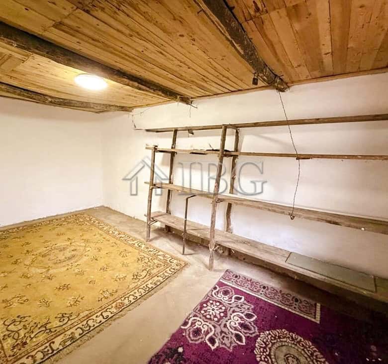 House interior with wooden ceiling and shelves, partially renovated with carpets on the floor.