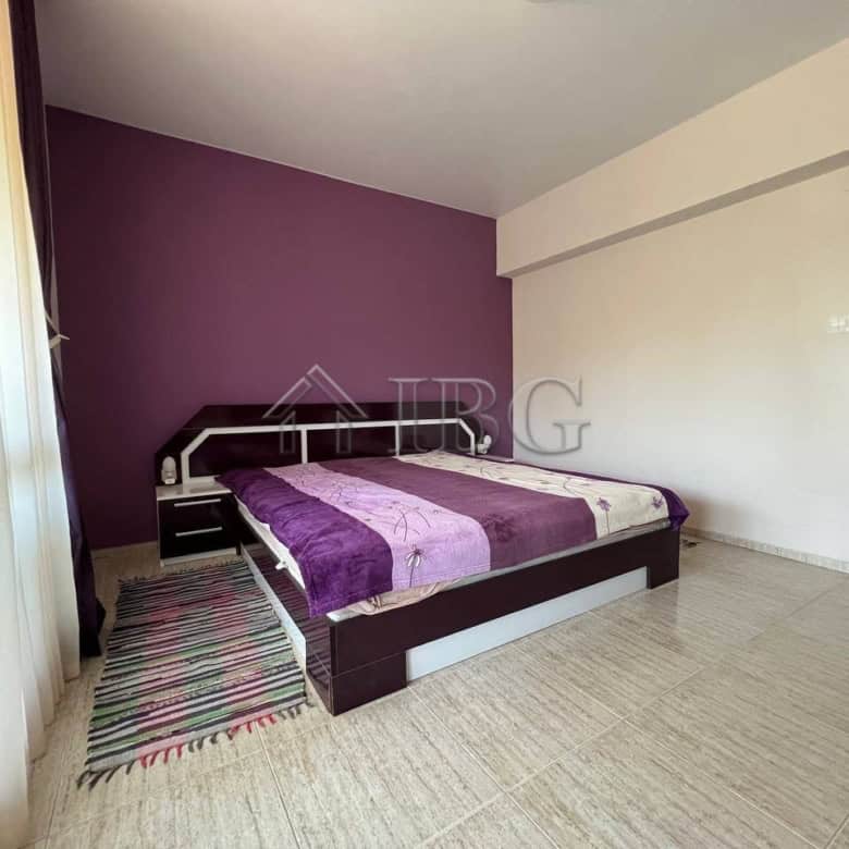 Bright bedroom with purple accent wall and large window in a modern apartment.