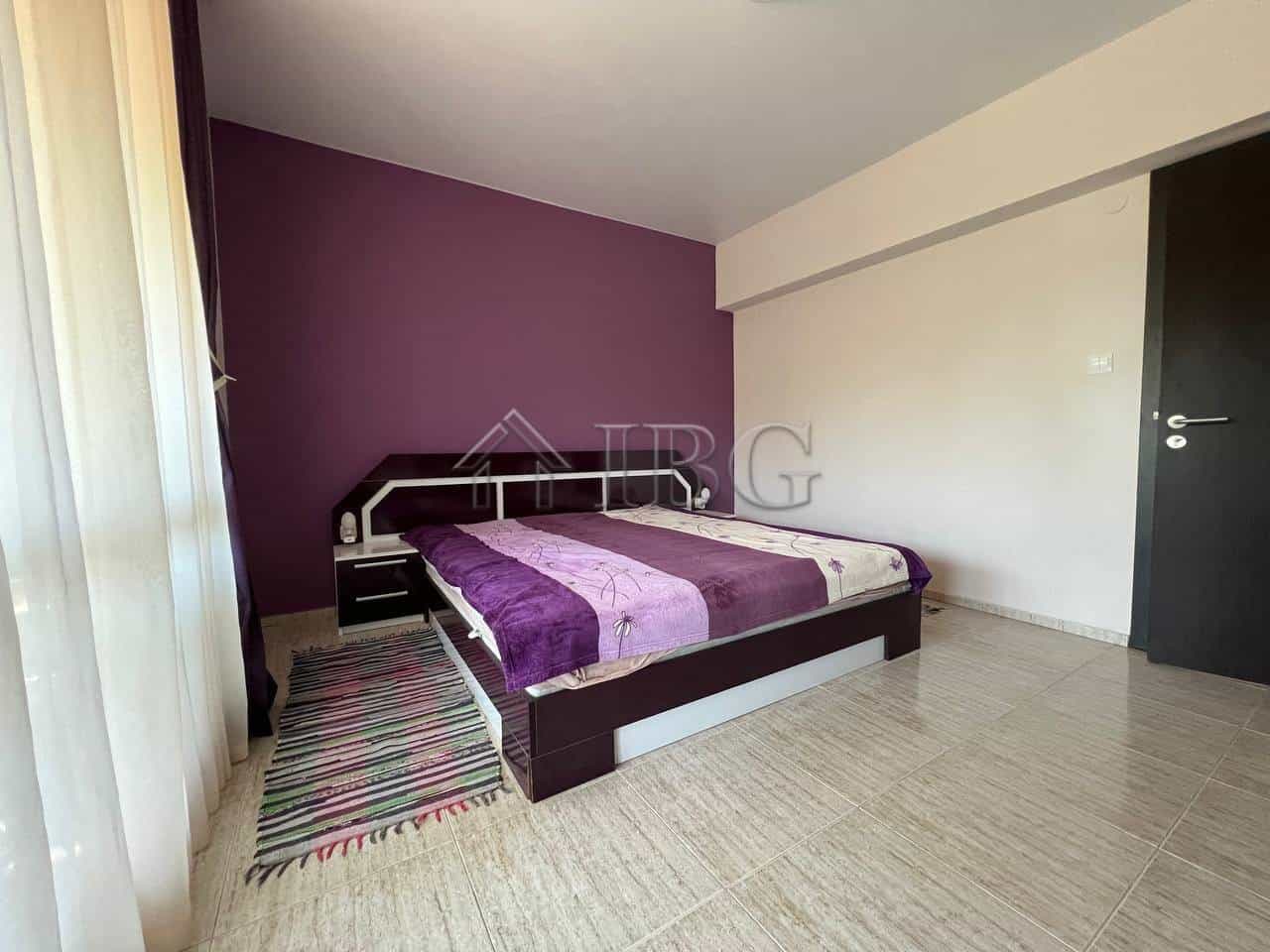 Bright bedroom with purple accent wall and large window in a modern apartment.