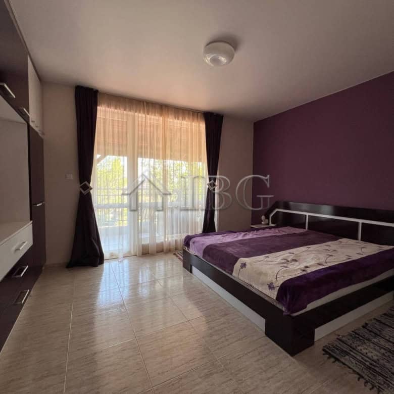 Spacious bedroom featuring a large bed, purple accent wall, and balcony overlooking the pool area in.