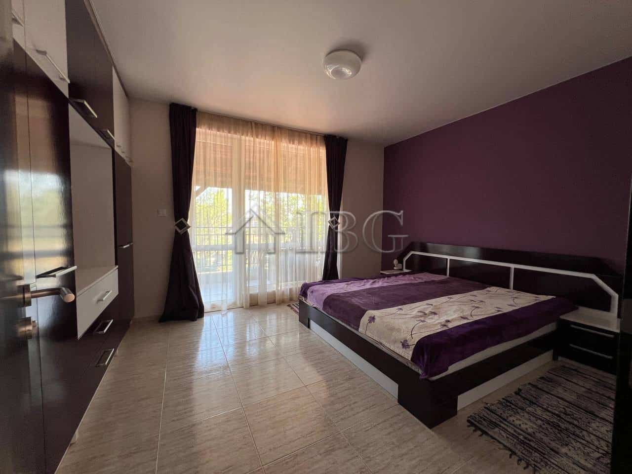 Spacious bedroom featuring a large bed, purple accent wall, and balcony overlooking the pool area in.