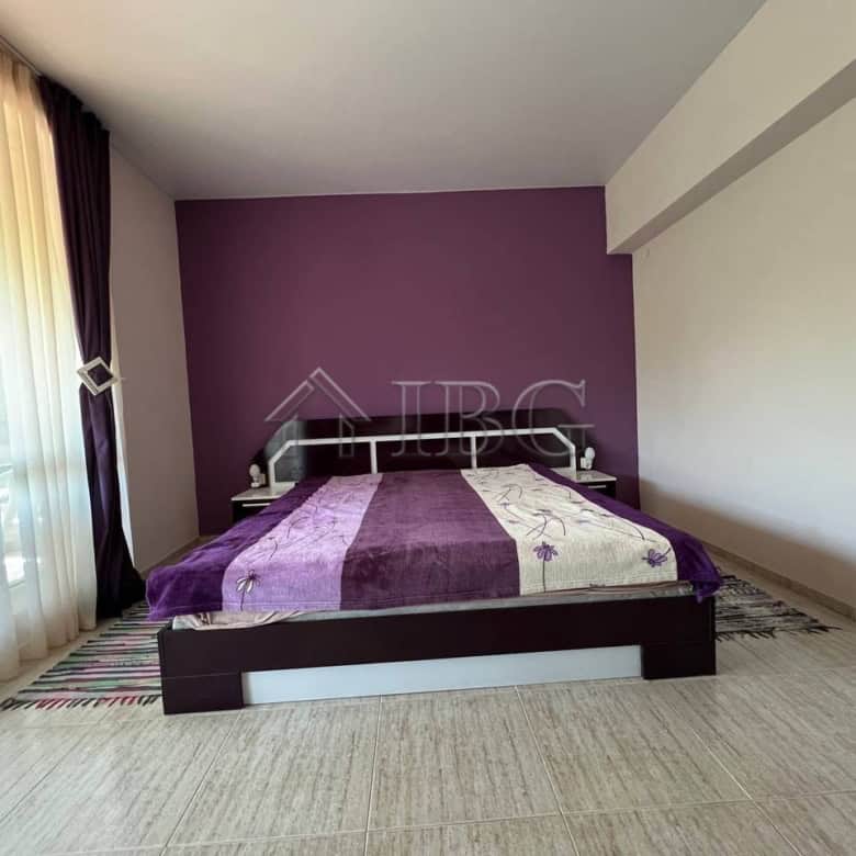 Bright bedroom with purple accent wall and large window with curtains.