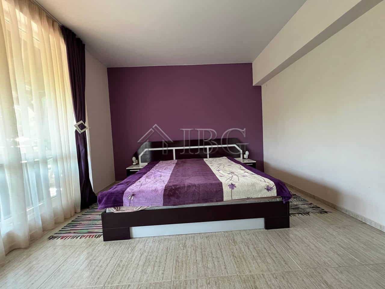 Bright bedroom with purple accent wall and large window with curtains.