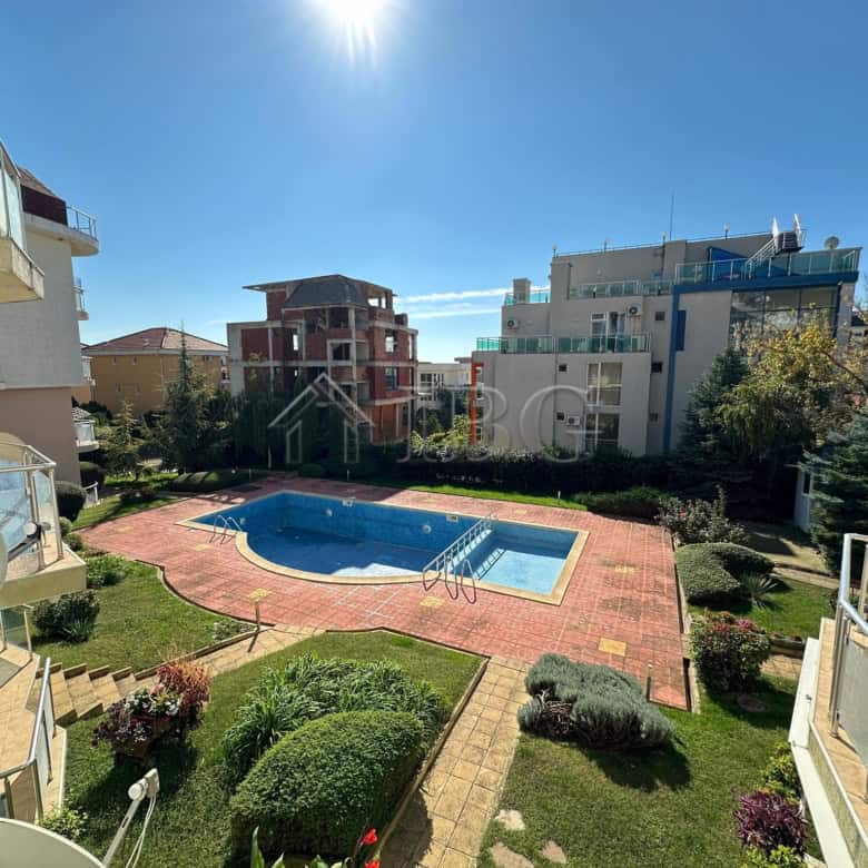 Bright view of the apartment complex with a swimming pool and surrounding greenery.
