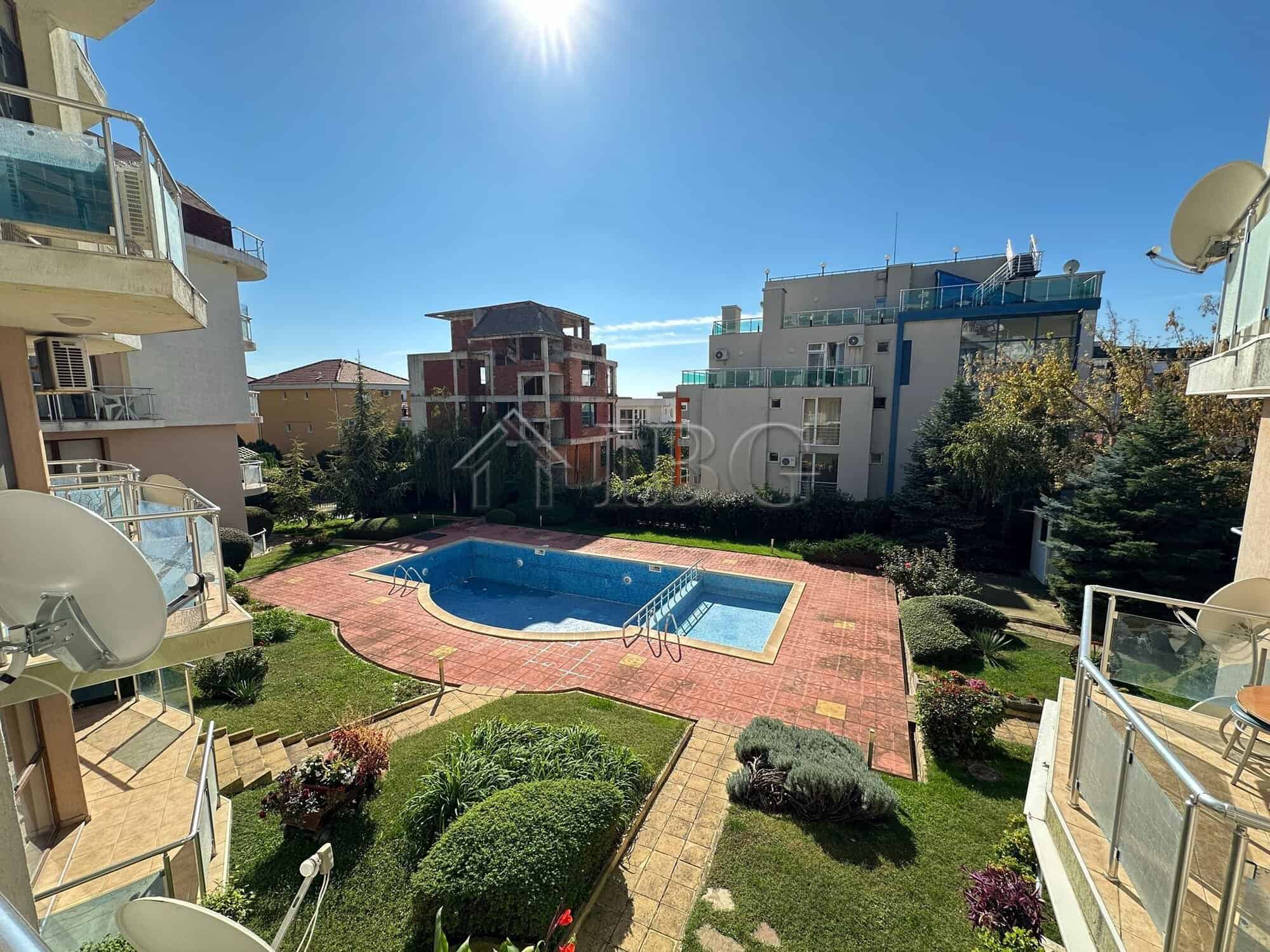 Bright view of the apartment complex with a swimming pool and surrounding greenery.