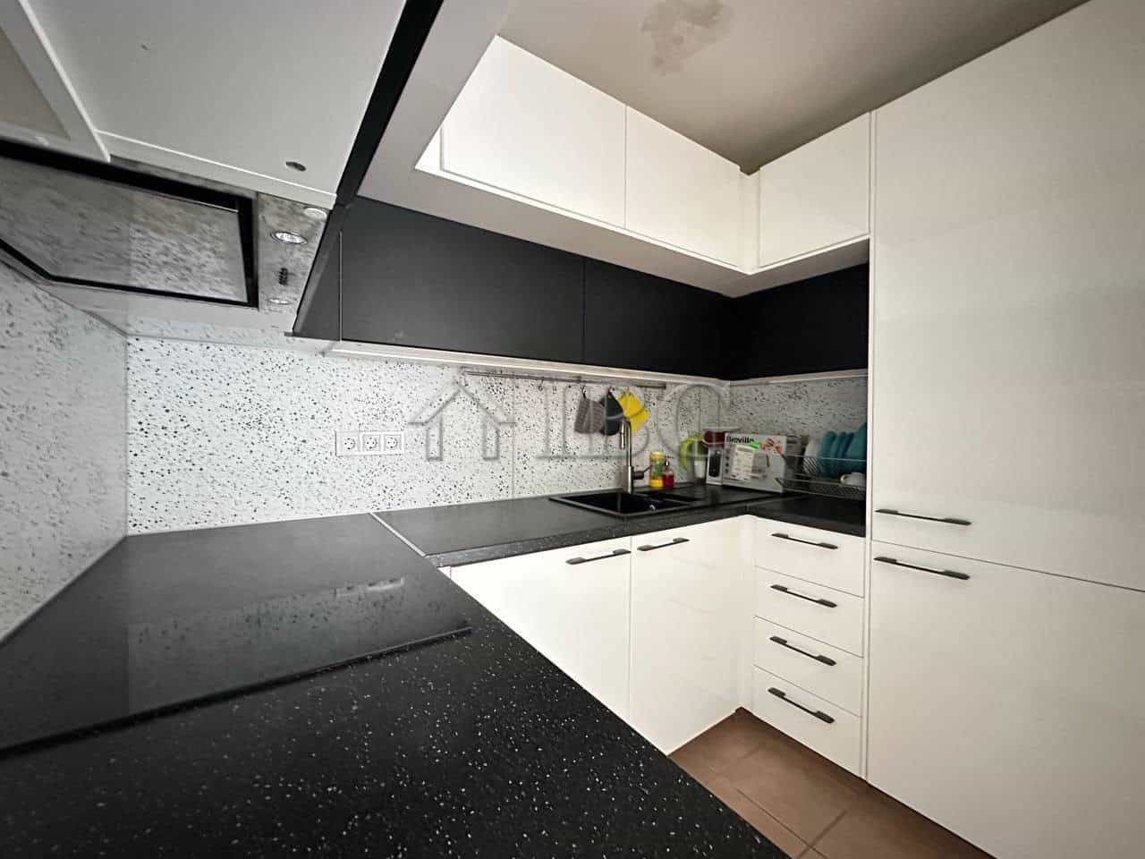 Contemporary kitchen with white cabinets and black countertops in Sveti Vlas apartment.