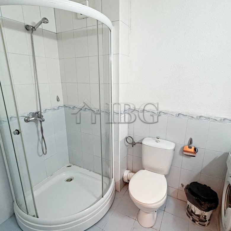 Bright bathroom featuring a glass shower enclosure, toilet, and washing machine in a modern apartmen.