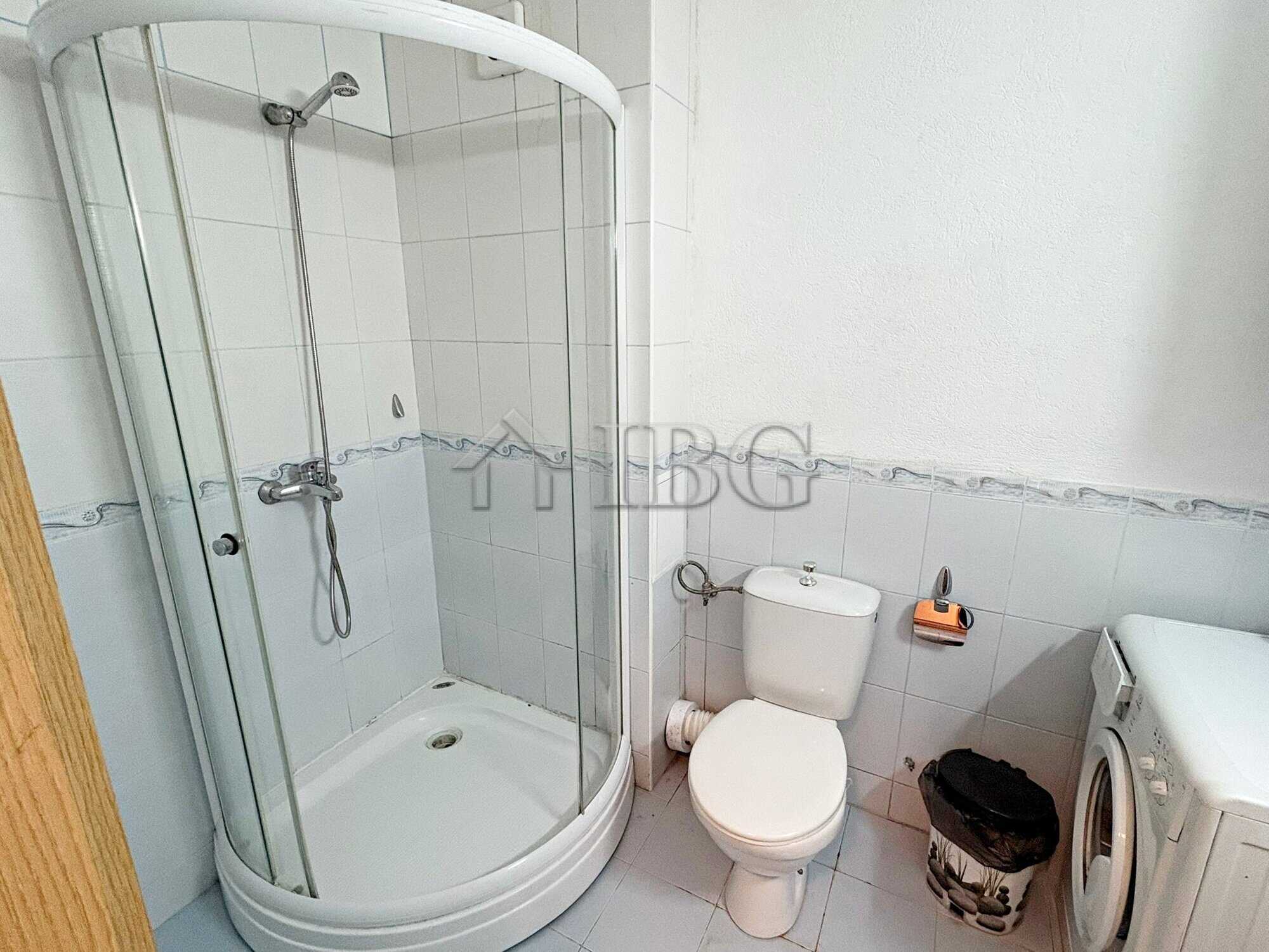 Bright bathroom featuring a glass shower enclosure, toilet, and washing machine in a modern apartmen.