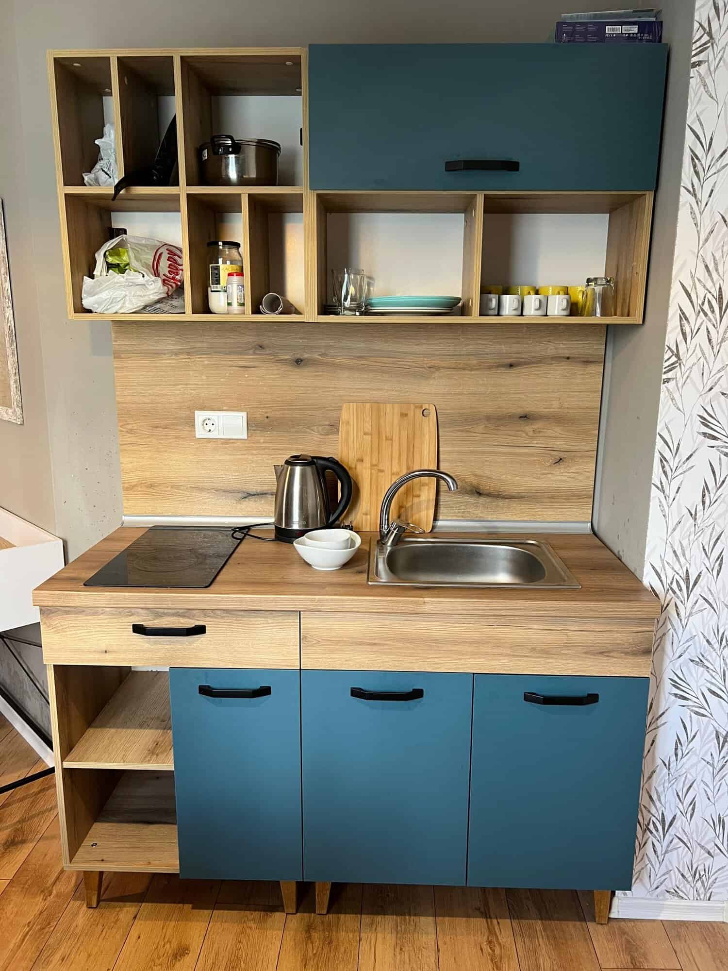 Compact studio kitchen with blue cabinets and open shelving in Saint Vlas.