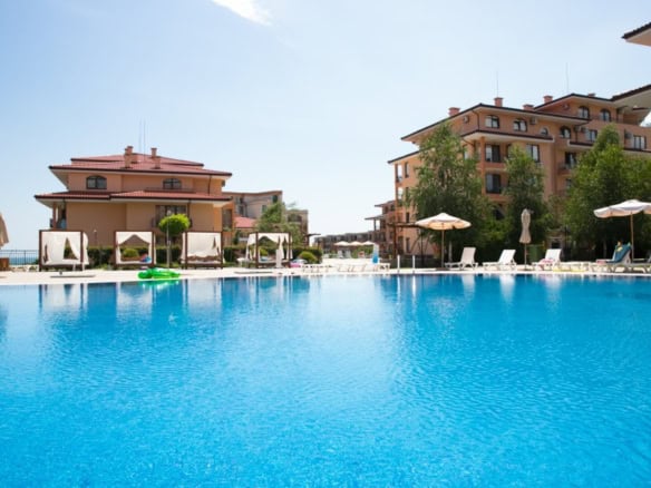 Bright outdoor pool area with sun loungers and umbrellas near residential buildings.