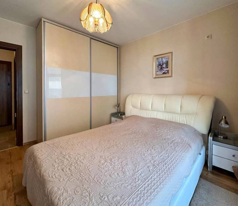 Spacious bedroom with a large wardrobe, comfortable bed, and warm lighting in a sunny apartment.