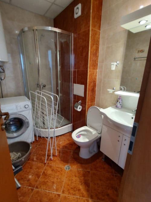 Compact bathroom featuring a glass shower enclosure, washing machine, and essential fixtures.