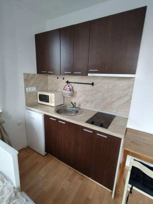 Compact kitchen with dark wood cabinets and essential appliances in a top-floor studio.