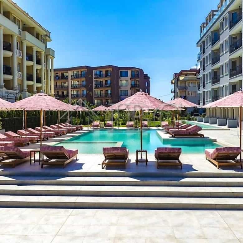 Pool with sun loungers and pink umbrellas in a modern residential complex.