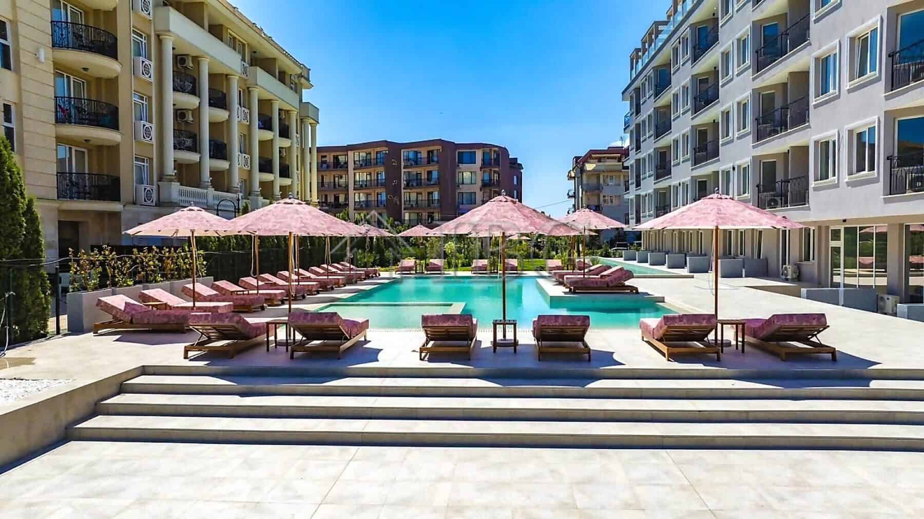 Pool with sun loungers and pink umbrellas in a modern residential complex.