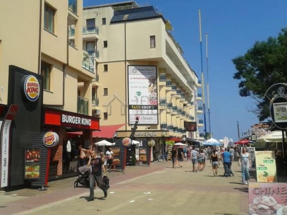 Bright street view of Kaya, Sunny Beach with a studio apartment building and commercial shops.