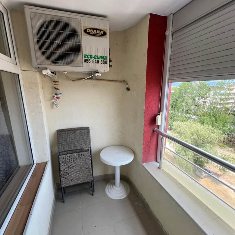 Balcony with air conditioning unit, small table, and view of greenery in Sunny Beach.
