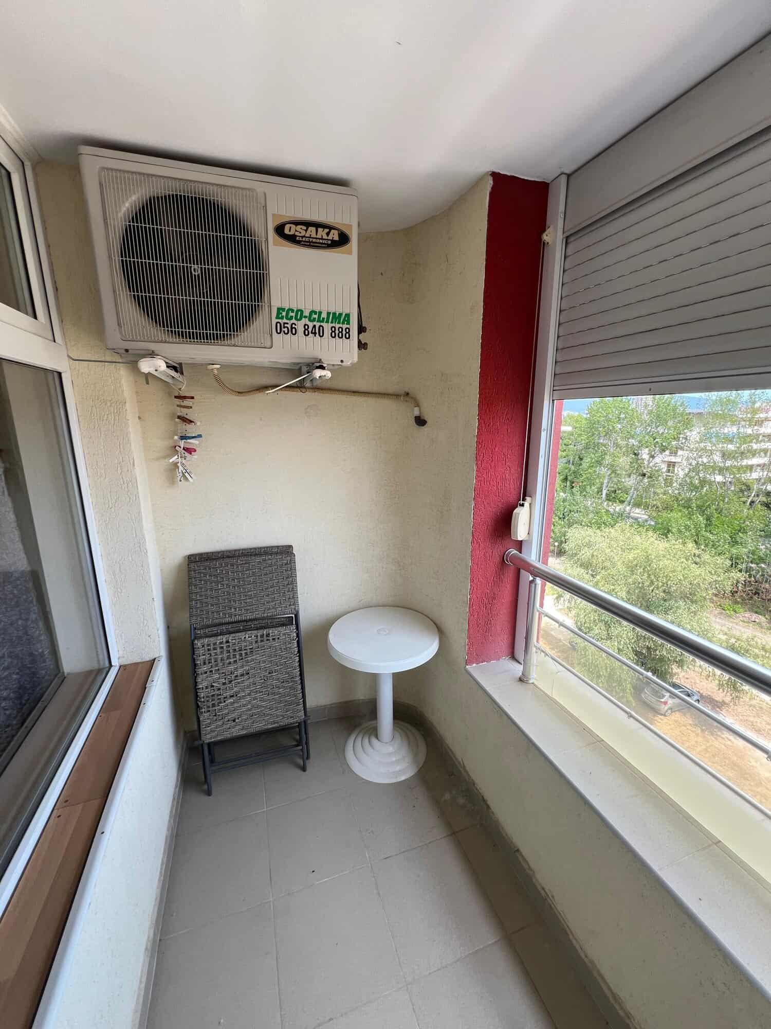 Balcony with air conditioning unit, small table, and view of greenery in Sunny Beach.