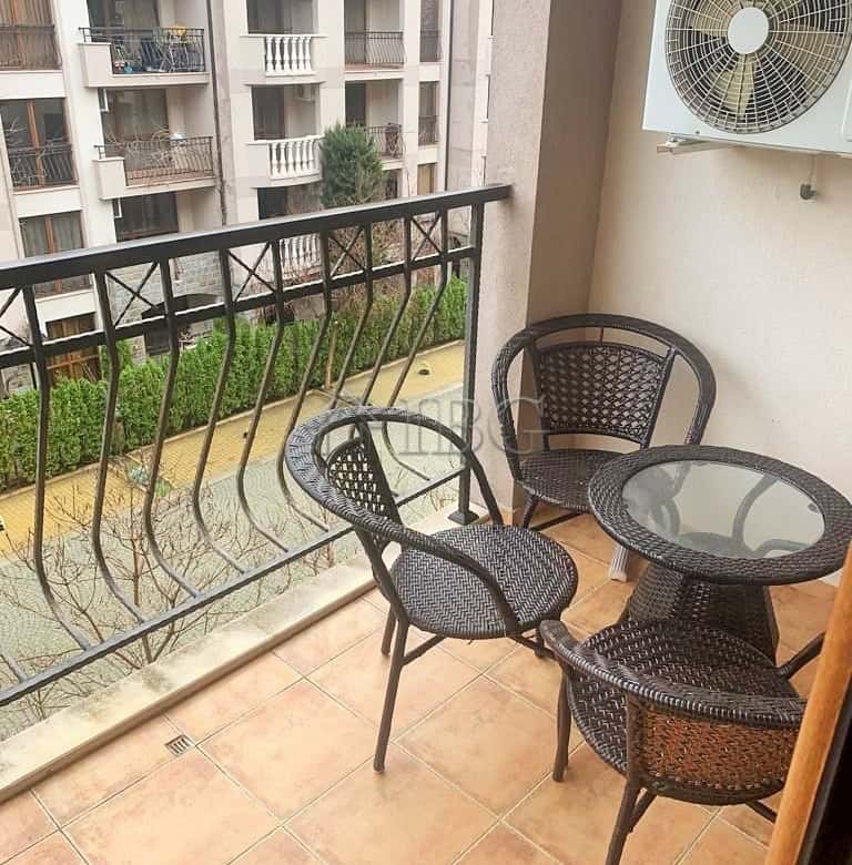 Balcony with a round glass table and four wicker chairs overlooking a residential complex.