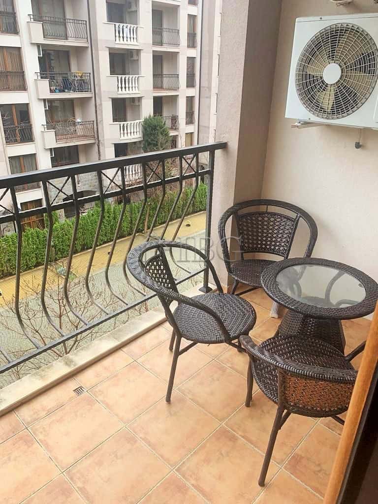 Balcony with a round glass table and four wicker chairs overlooking a residential complex.