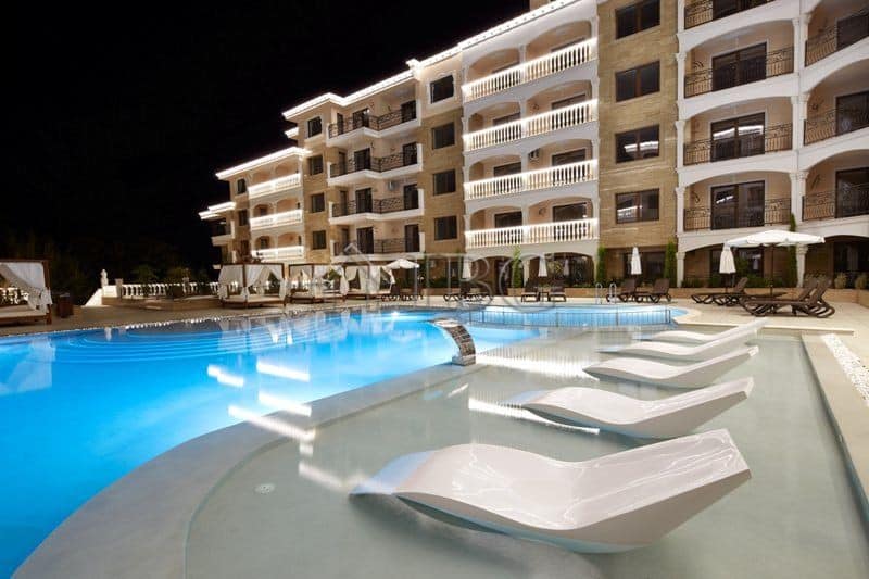 Pool view of a modern apartment building with lounge chairs and umbrellas.
