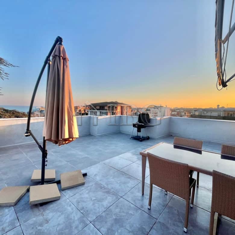 Rooftop terrace with outdoor furniture and umbrella overlooking Ravda coastline.