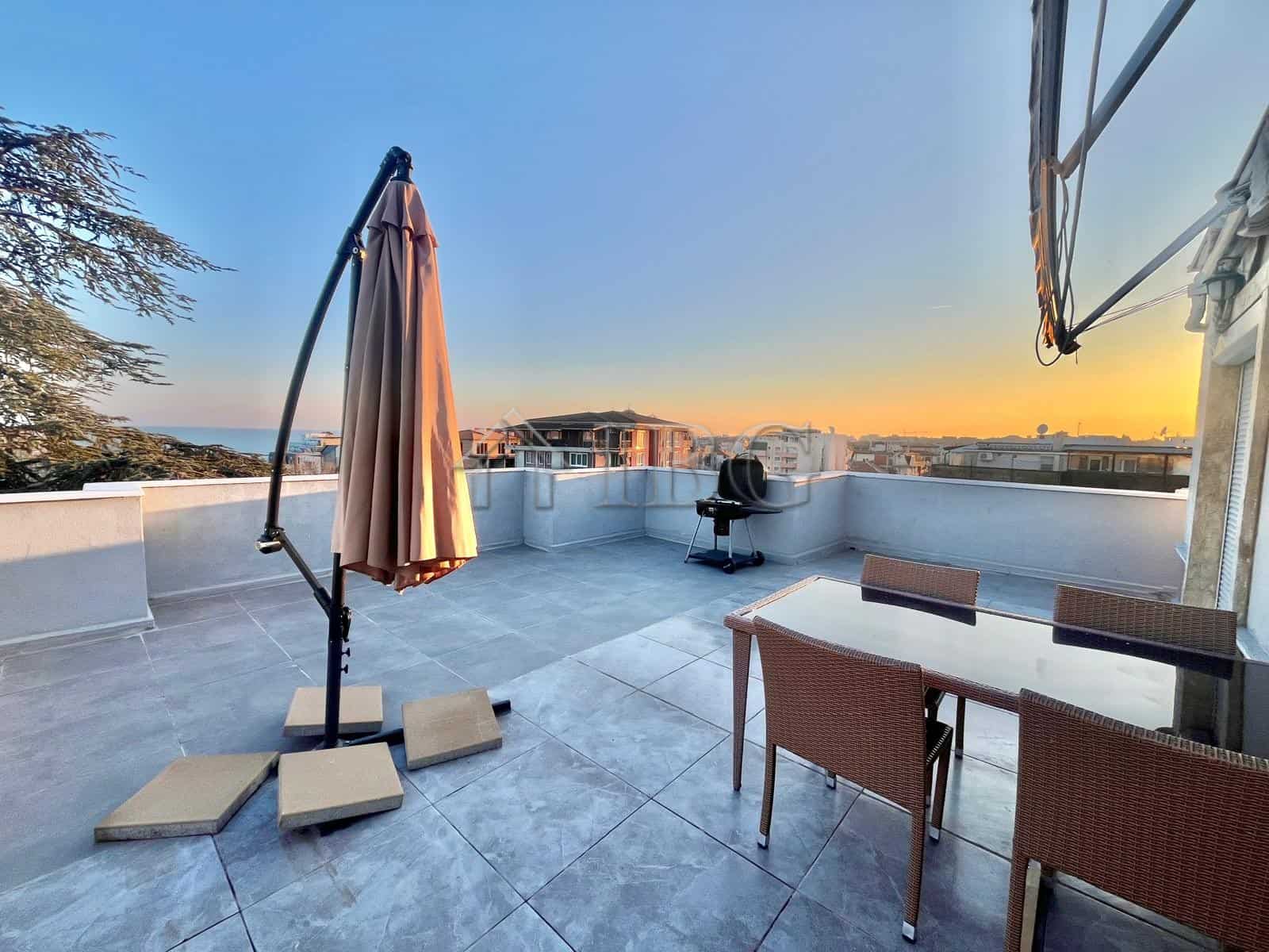 Rooftop terrace with outdoor furniture and umbrella overlooking Ravda coastline.